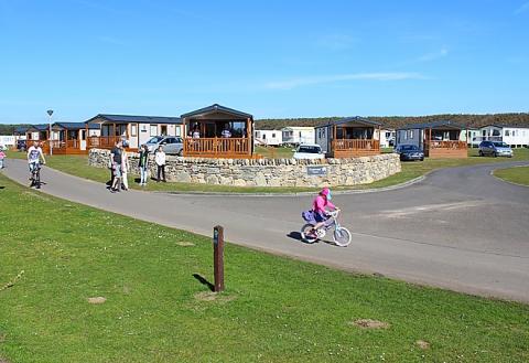 Family strolling and cycling past holiday homes in the sunshine