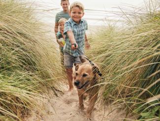 Happy family walking small dog between sand dunes