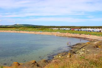 Children paddling in the shallow, calm sea on the beach at Elie Holiday Park, Shell Bay on a sunny day
