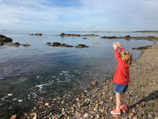 Girl throwing pebbles into the sea at Largo Bay