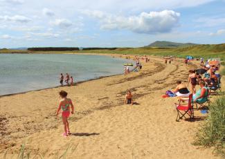 Children paddling in the shallow, calm sea on the beach at Elie Holiday Park, Shell Bay on a sunny day
